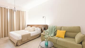 A bedroom with a bed, a green sofa, a small table with a vase, and a lamp.