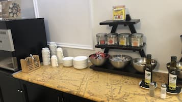 Un comptoir de cuisine avec une machine à café, une pile d’assiettes, des bols et des pots à condiments.