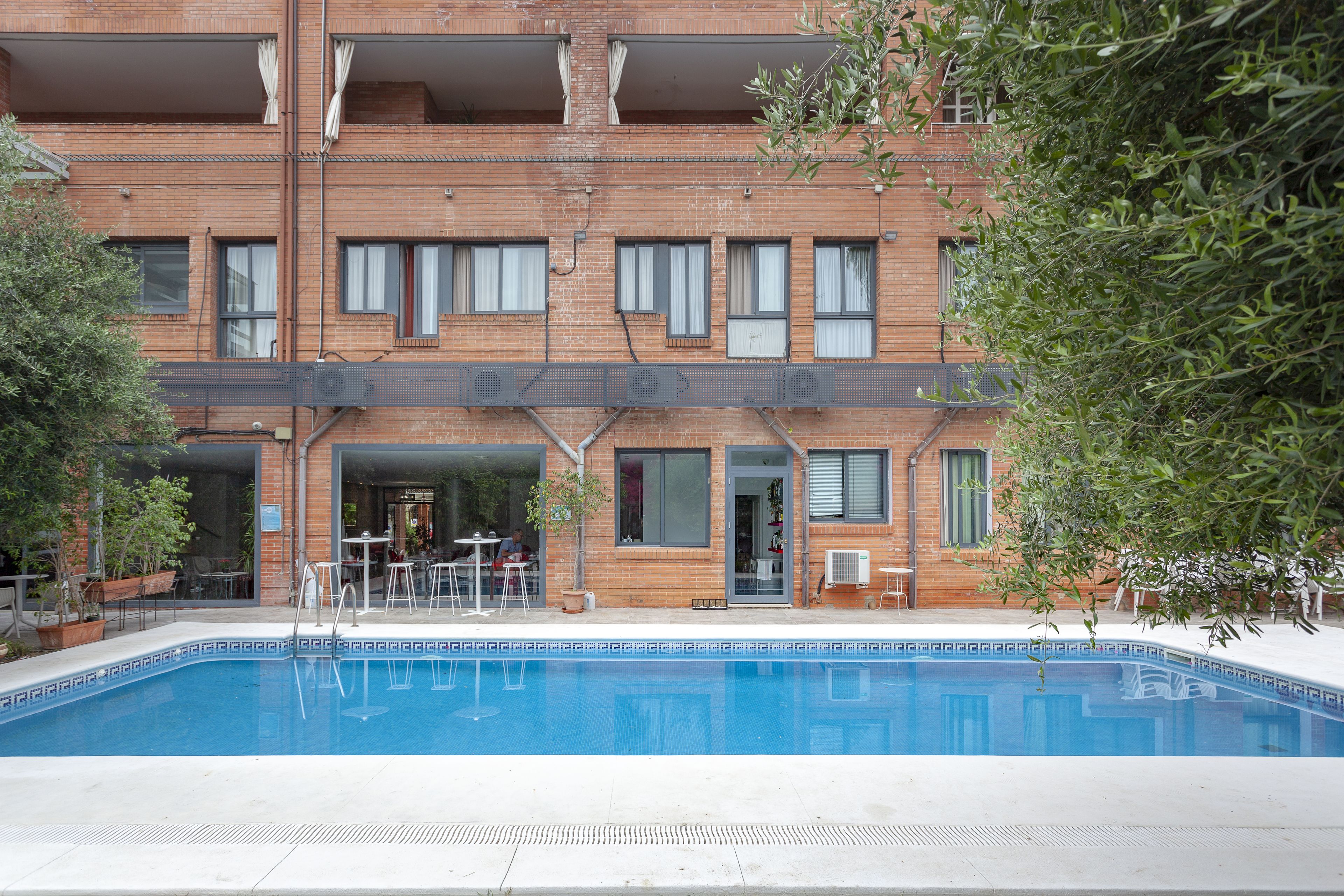 Area piscina con un edificio in mattoni sullo sfondo, posti a sedere all'aperto e una pianta in vaso.