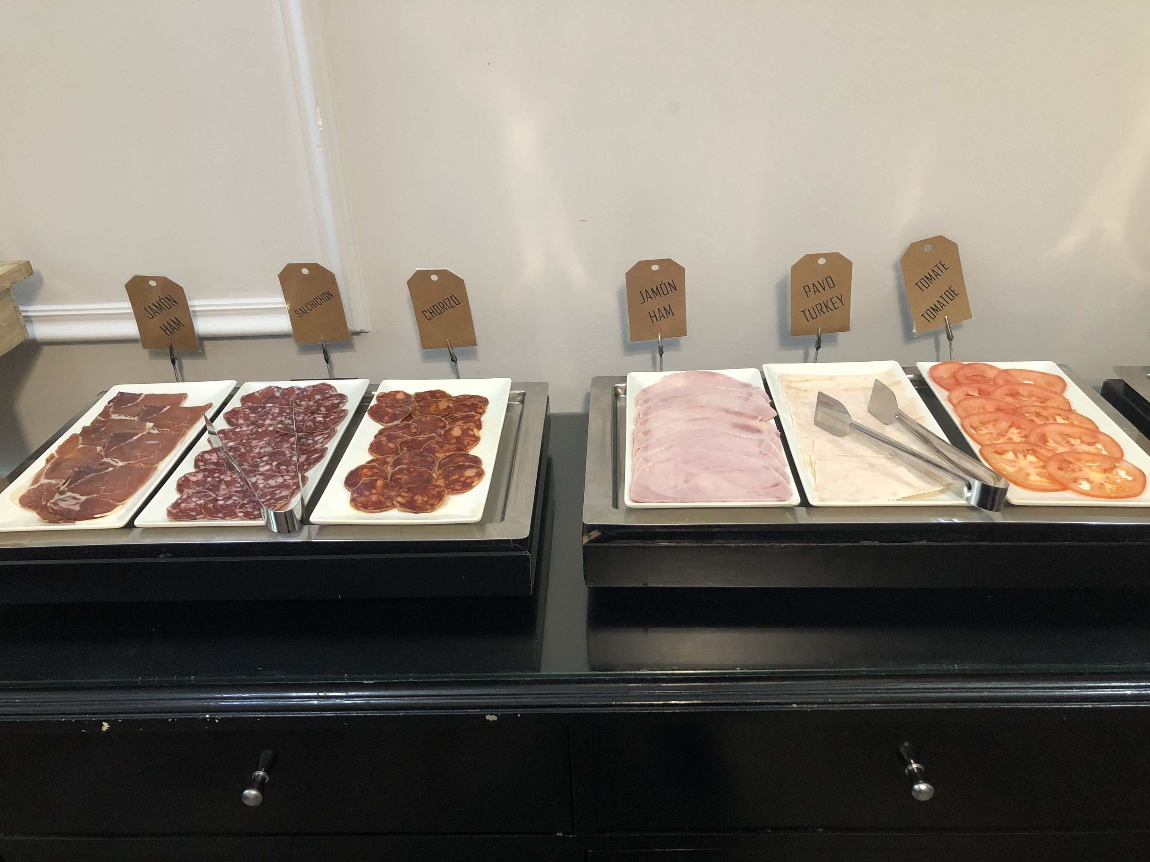 Mostrador de charcutería con diversos tipos de carnes y tomates etiquetados.