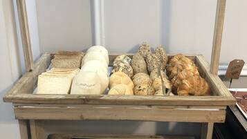 Een bakkerijvitrine met verschillende broden en gebak, inclusief een bordje met de tekst 'Pan - Bread'.