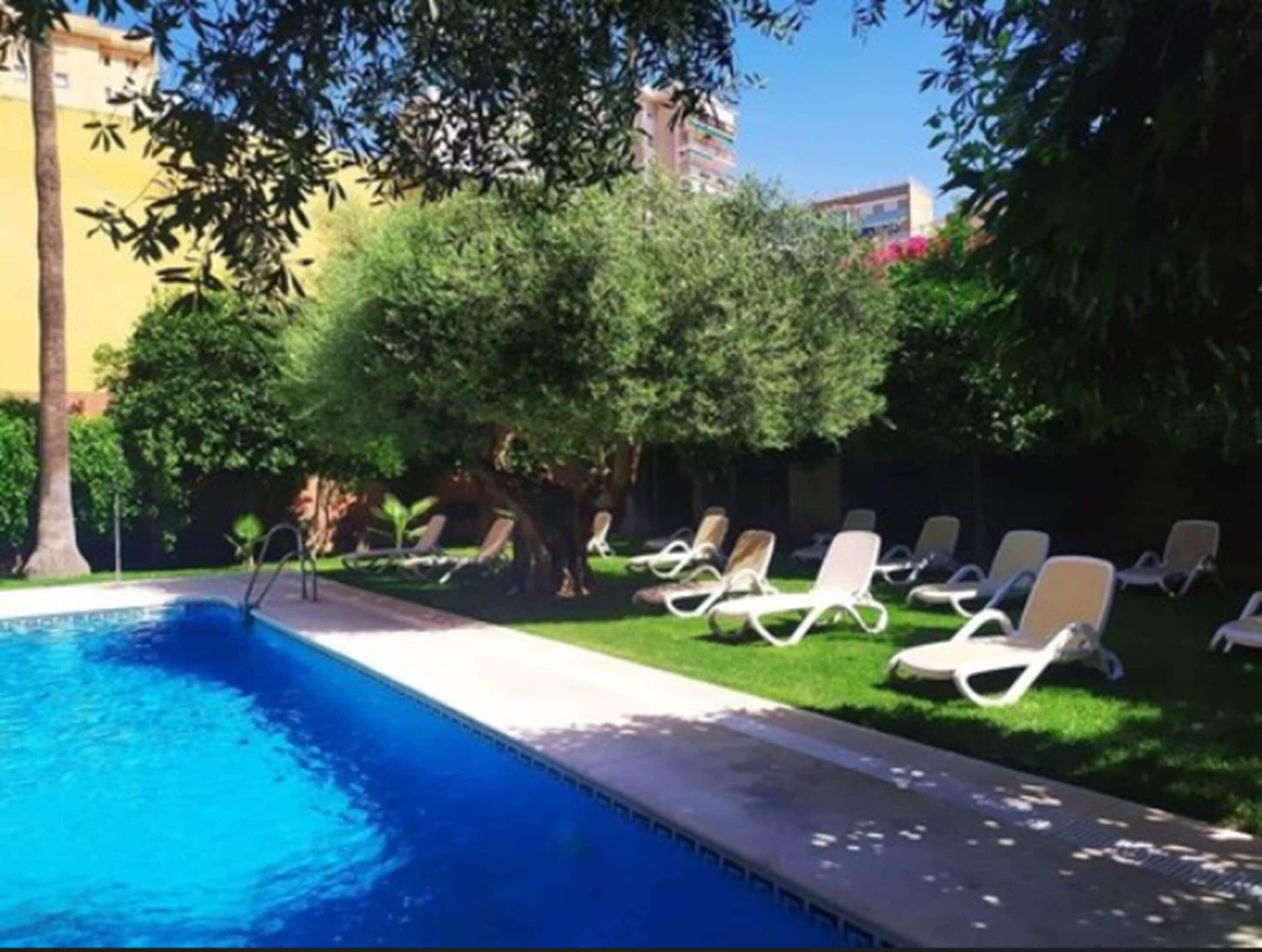 A swimming pool with lounge chairs and greenery.