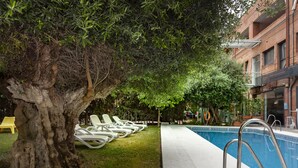 A poolside area with lounge chairs, a tree, and a building in the background. - Hotel AACR Monteolivos (Seville)