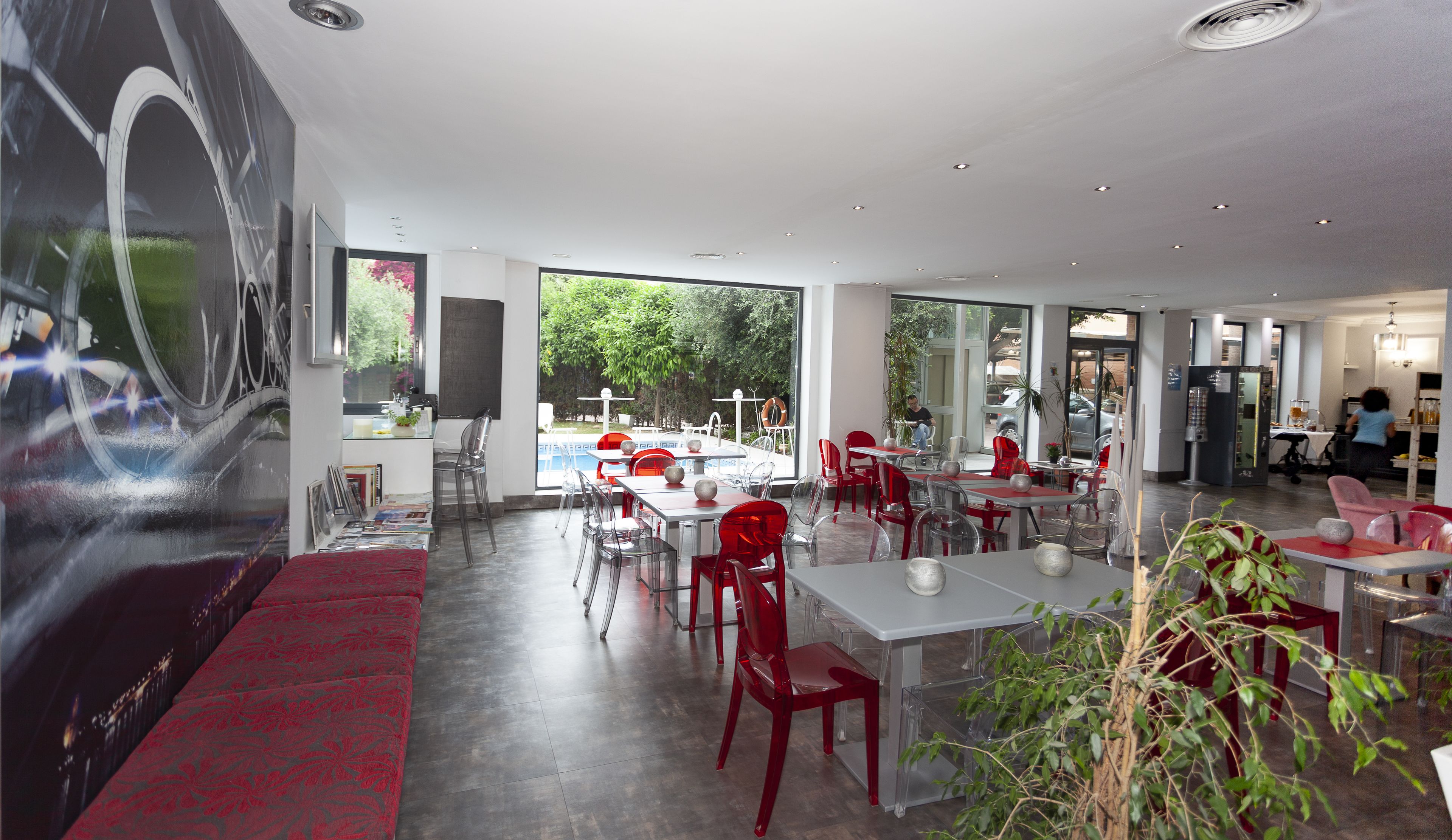 Un restaurante moderno con vista a una piscina, sillas de vidrio transparente y una zona con alfombra roja.