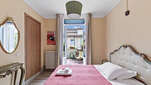 Ein Schlafzimmer mit Bett, Spiegel, Heizkörper und einer offenen Tür zu einem Außenbereich.