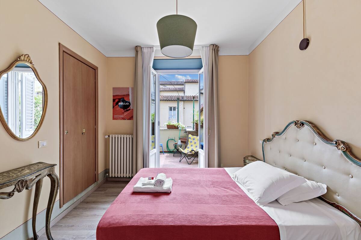 Un dormitorio con cama, espejo, radiador y puerta abierta que da a un espacio exterior.