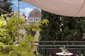 A balcony with a view of a building with a dome, surrounded by greenery.