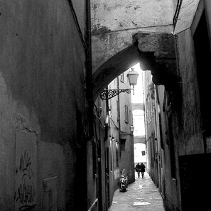 A narrow alleyway with a motorcycle parked at the end, flanked by buildings with visible graffiti and a street lamp overhead. - Hotel Cestelli (Florence)