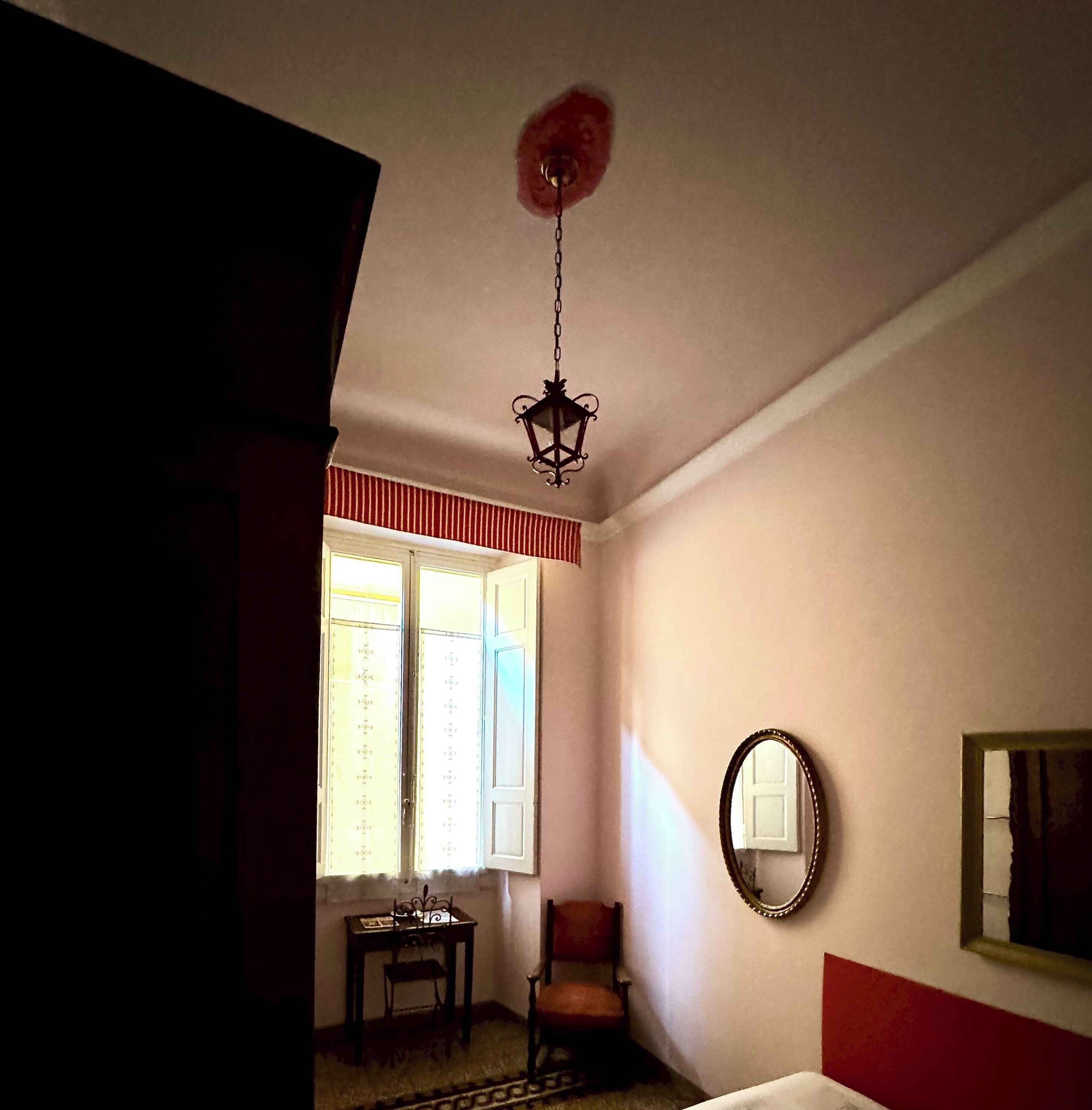 A room with a bed, a chair, a table, a mirror, and a window with curtains.