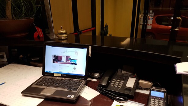 Un bureau avec un ordinateur portable, un téléphone de bureau, un téléphone portable, une souris d’ordinateur verte et une plante en pot.