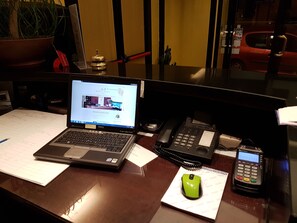 A desk with a laptop, a desktop phone, a mobile phone, a green computer mouse, and a potted plant. - Albergo Sonia (Florence)