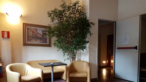 Un hall d’entrée avec un comptoir de réception, deux fauteuils, une petite table, une plante en pot, un tableau encadré et une porte avec une pancarte.