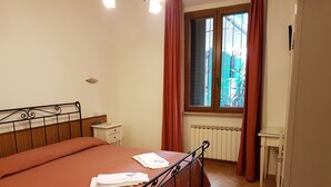 Une chambre à coucher avec un lit, une table de chevet, une fenêtre avec des rideaux et un radiateur.