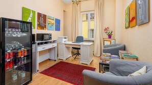 Een compacte leefruimte met een kitchenette, een bureau, een grijze bank en kunstwerken aan de wanden.