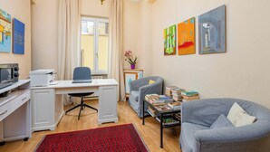 Een kamer met een bureau, een bureaustoel, twee fauteuils, een boekenkast en kunstwerken aan de wanden.