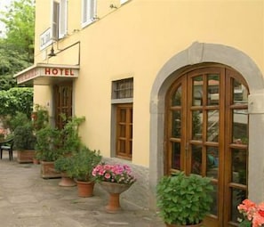 A hotel with a yellow facade, a signboard with "HOTEL" written on it, and a large arched window. There are potted plants in front of the building. - Calzaiolo (San Casciano in Val di Pesa)