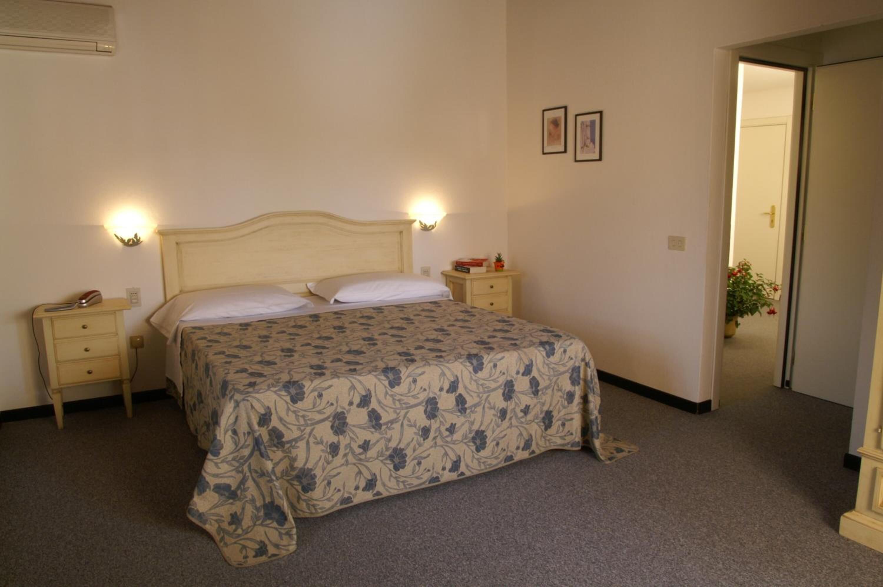 Un dormitorio con cama, mesitas de noche y una puerta que da a otra habitación.