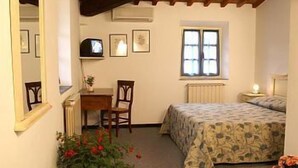 Un dormitorio pequeño y acogedor con cama, escritorio y silla. Hay una ventana con vistas al exterior y una planta en maceta sobre el suelo.