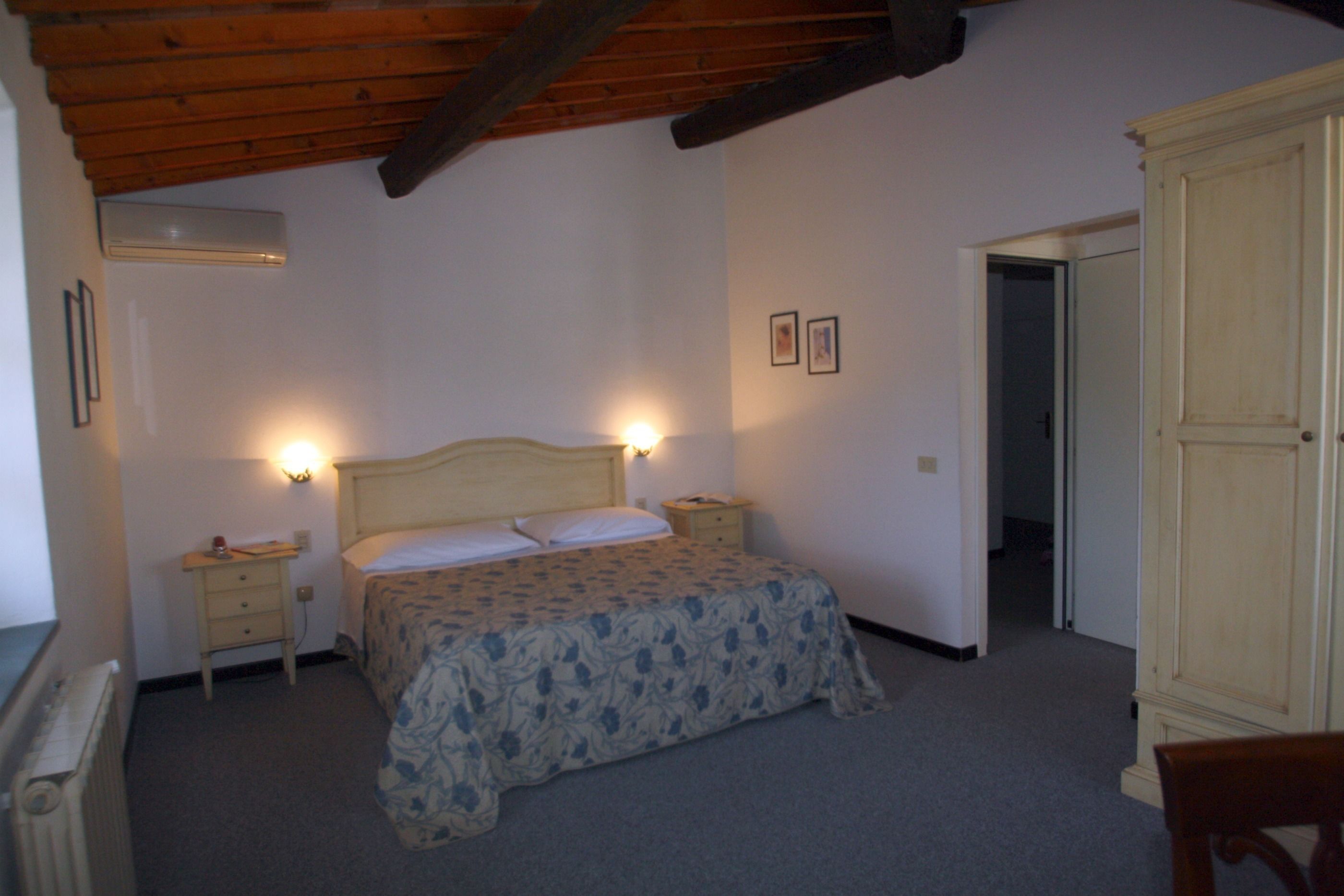 A bedroom with a bed, bedside tables, a wardrobe, and a door leading to another room.