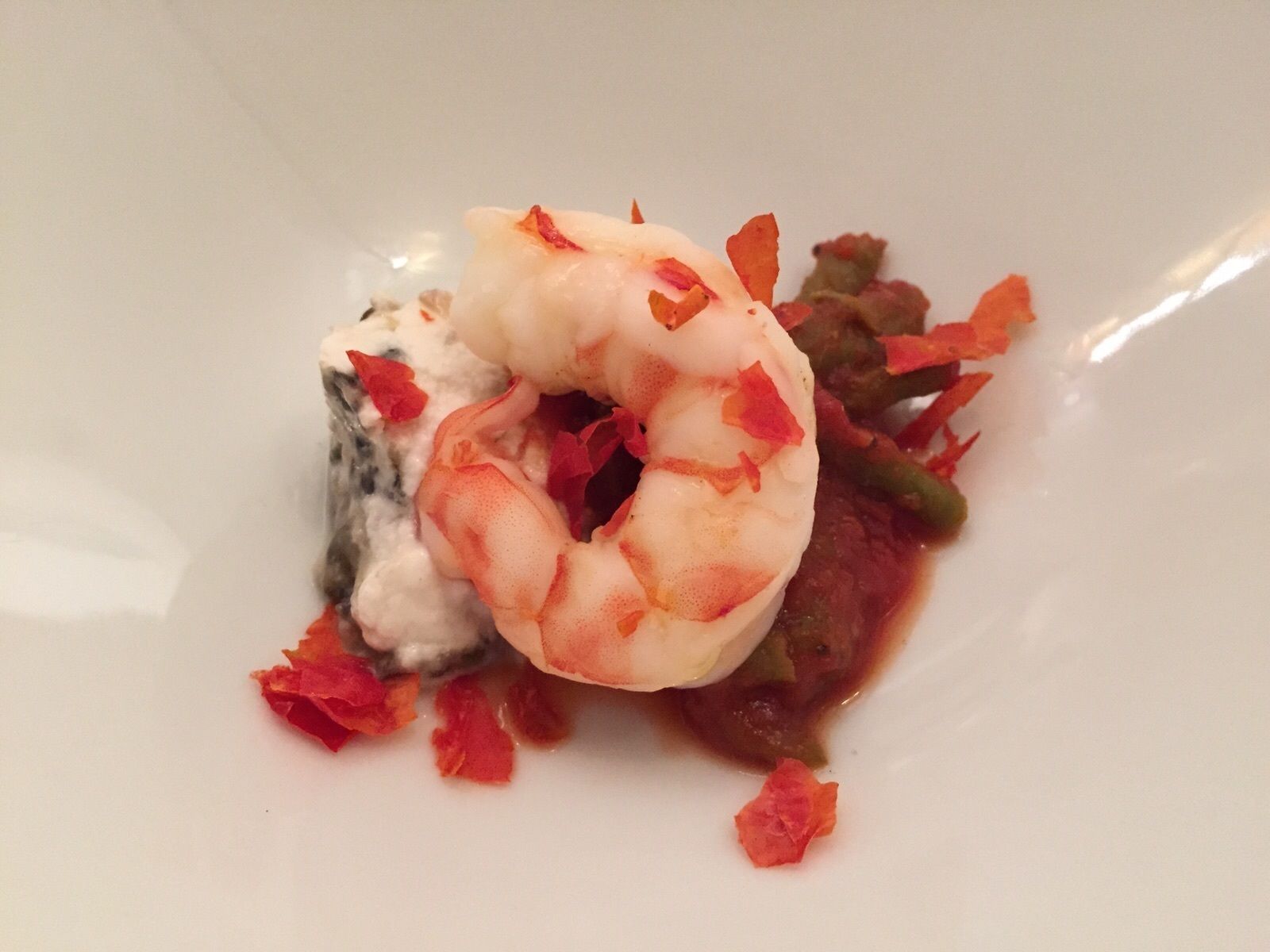 A plate with a shrimp, some greens, and a creamy substance.