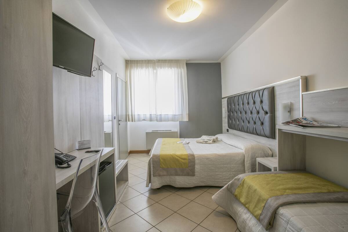 A hotel room with two beds, a desk with a chair, a television, and a window with curtains.