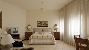 A hotel room with a bed, a television, a lamp, a painting, and a dining table.