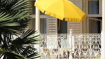 Een balkon met een gele parasol, witte reling en een groene muur.