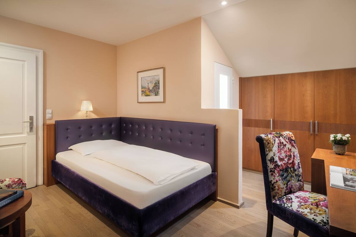 A bedroom with a bed, a chair, a desk, and a painting on the wall.