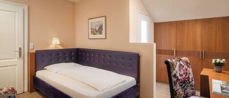A bedroom with a bed, a chair, a desk, and a painting on the wall.