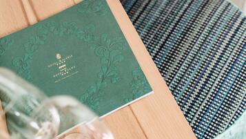A green hotel brochure with embossed text, a glass, and a patterned cushion.
