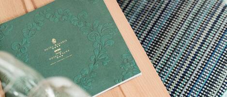 A green hotel brochure with embossed text, a glass, and a patterned cushion.
