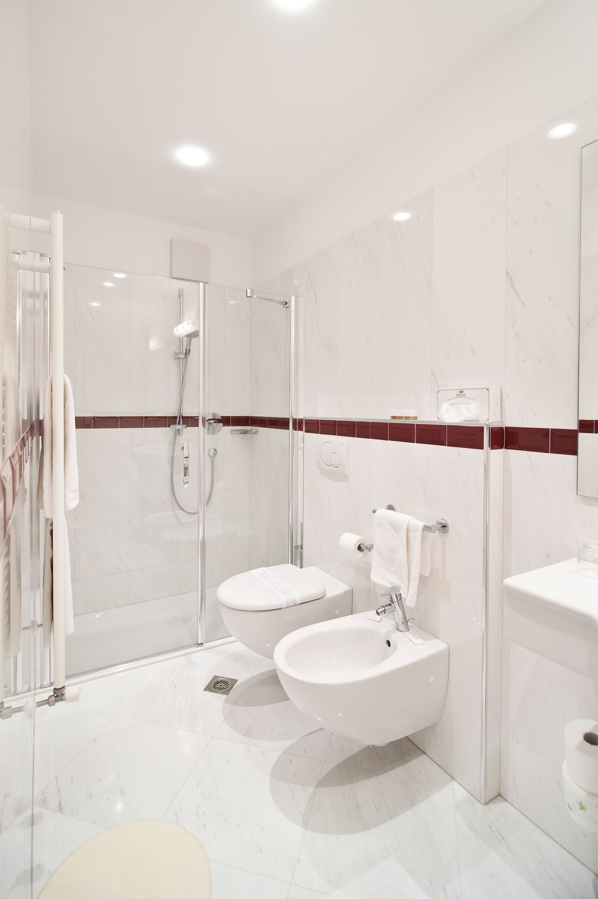 Et moderne badeværelse med et glasvæg-afskærmet brusebad, to håndvaske og et toilet.