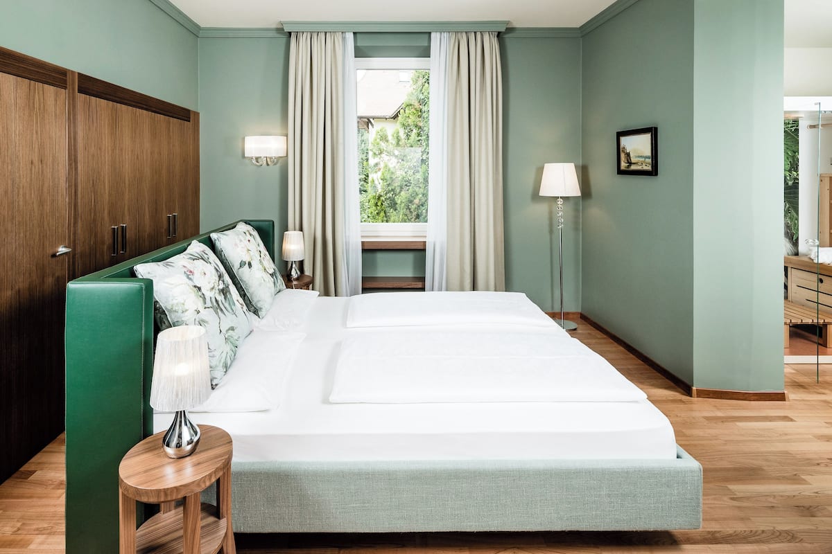 A bedroom with a bed, a nightstand, a lamp, a wardrobe, and a window with curtains.