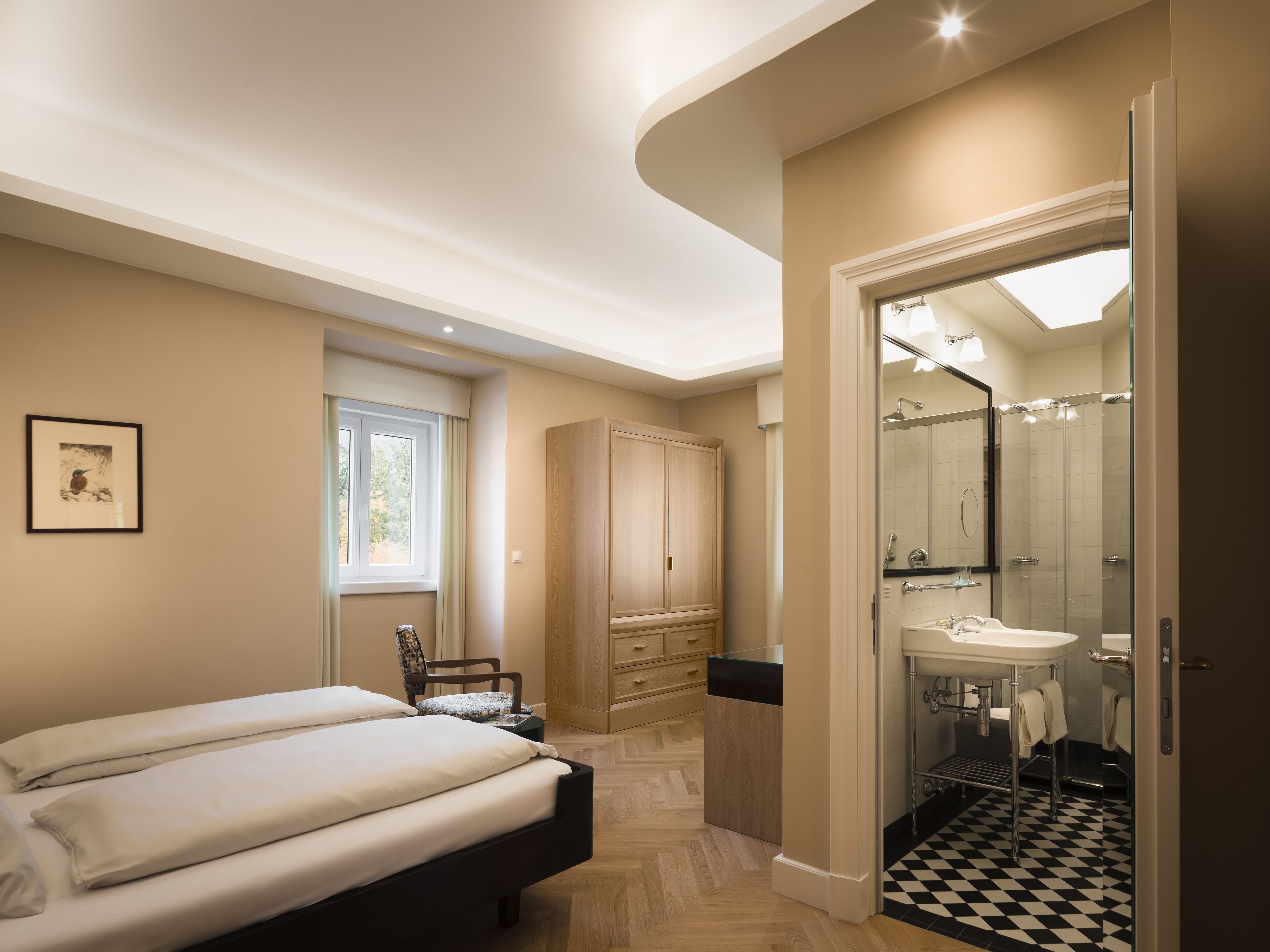 A bedroom with a bed, a chair, a wardrobe, and a bathroom with a sink and mirror.