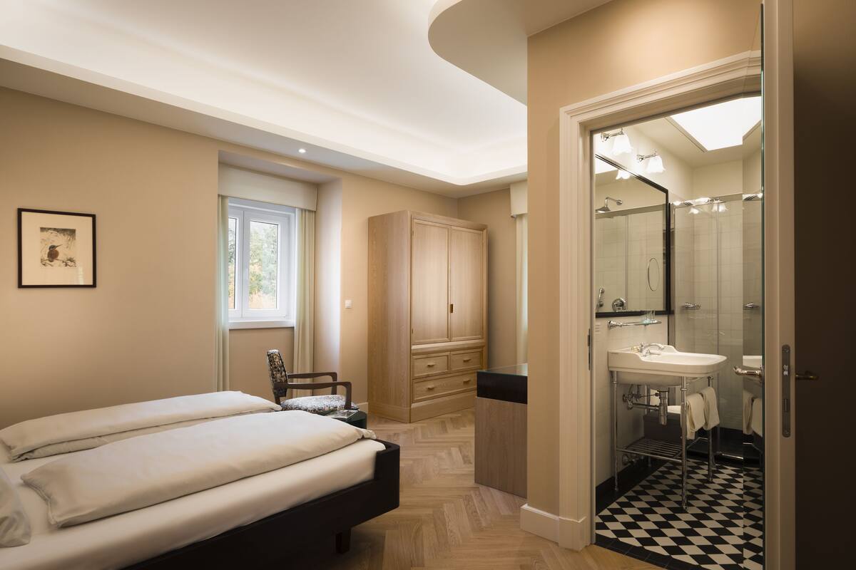 A bedroom with a bed, a chair, a wardrobe, and a bathroom with a sink and mirror.