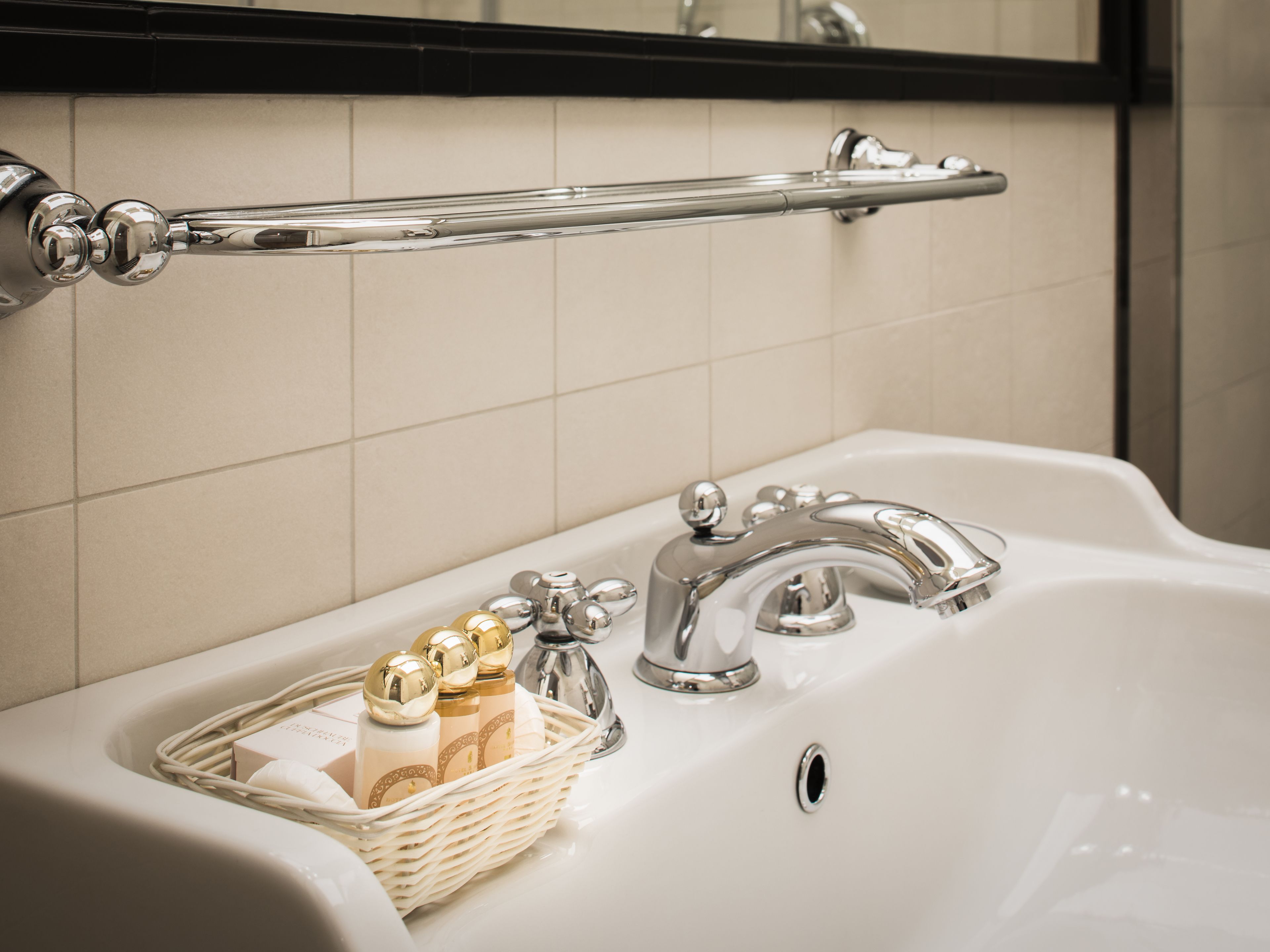 A bathroom sink with a chrome faucet, a chrome towel rack, and a wicker basket containing toiletries.