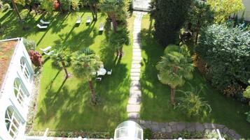 An aerial view of a well-maintained garden with a stone pathway, palm trees, and outdoor seating areas.