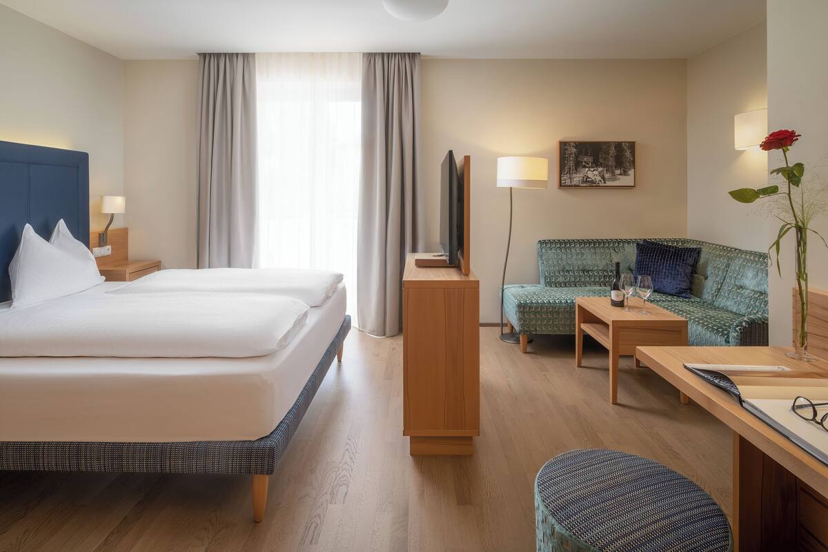A hotel room with a large bed, a desk, a chair, a TV, and a painting on the wall.