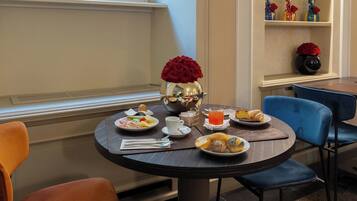 Une table ronde où sont disposés des plats de nourriture, un vase de roses rouges et un verre de jus d’orange.