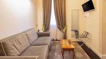 A living room with a sofa, a wooden coffee table, a TV mounted on the wall, and a chair.