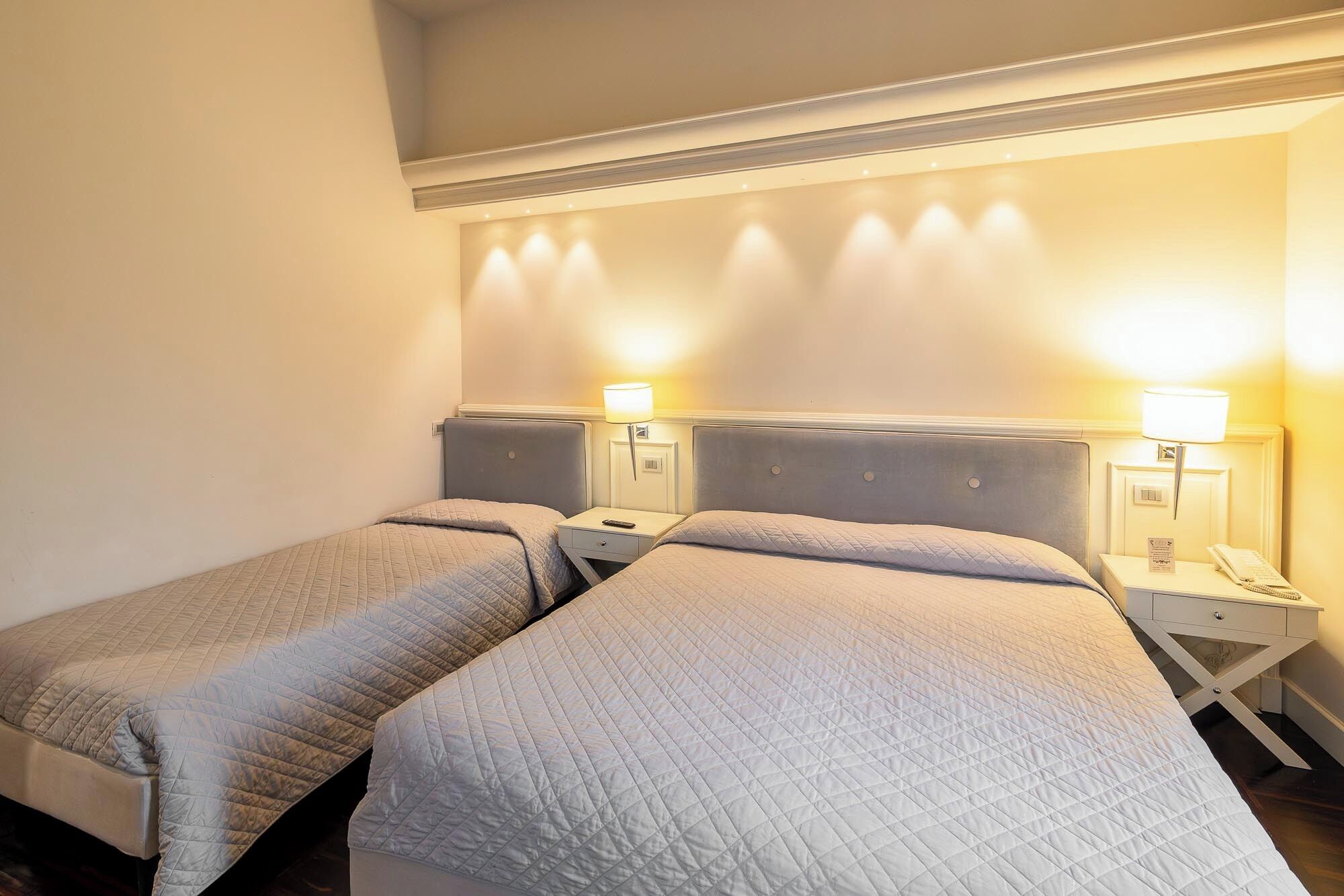 A hotel room with two single beds, each with a nightstand and a lamp.