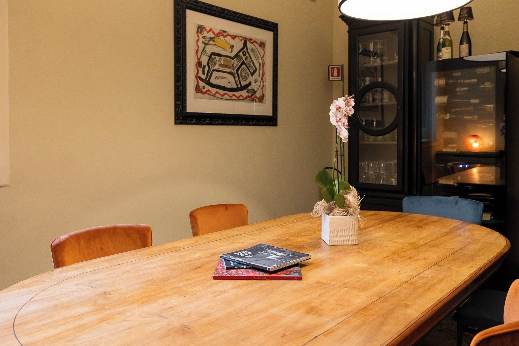 A wooden dining table with books, a vase with flowers, and a framed abstract artwork on the wall.