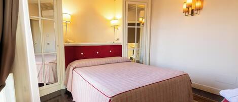 Un dormitorio con cama, espejo, mesita de noche y lámpara de pared.