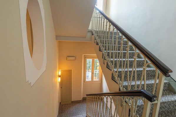 A staircase with patterned carpet and white railings, leading to a door with a window. - Hotel Patria (Pistoia)