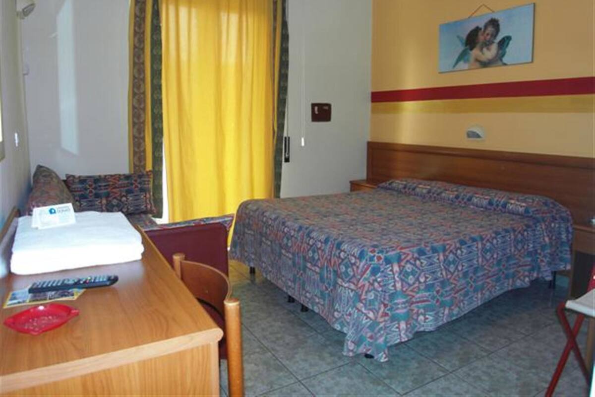 A hotel room with a bed, a desk with a chair, a telephone, and a window with curtains.