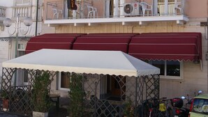 A hotel with multiple balconies, outdoor seating, and a covered patio area. - Hotel Dolly (Viareggio)