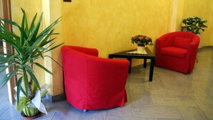 A room with a yellow wall, a potted plant, two red chairs, and a small table with a flower arrangement. - Hotel Dolly (Viareggio)