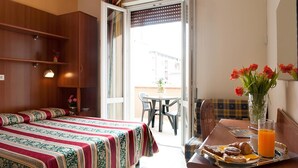 A hotel room with a bed, a dining table with breakfast items, a vase with flowers, and a view of the outside. - Hotel Dolly (Viareggio)