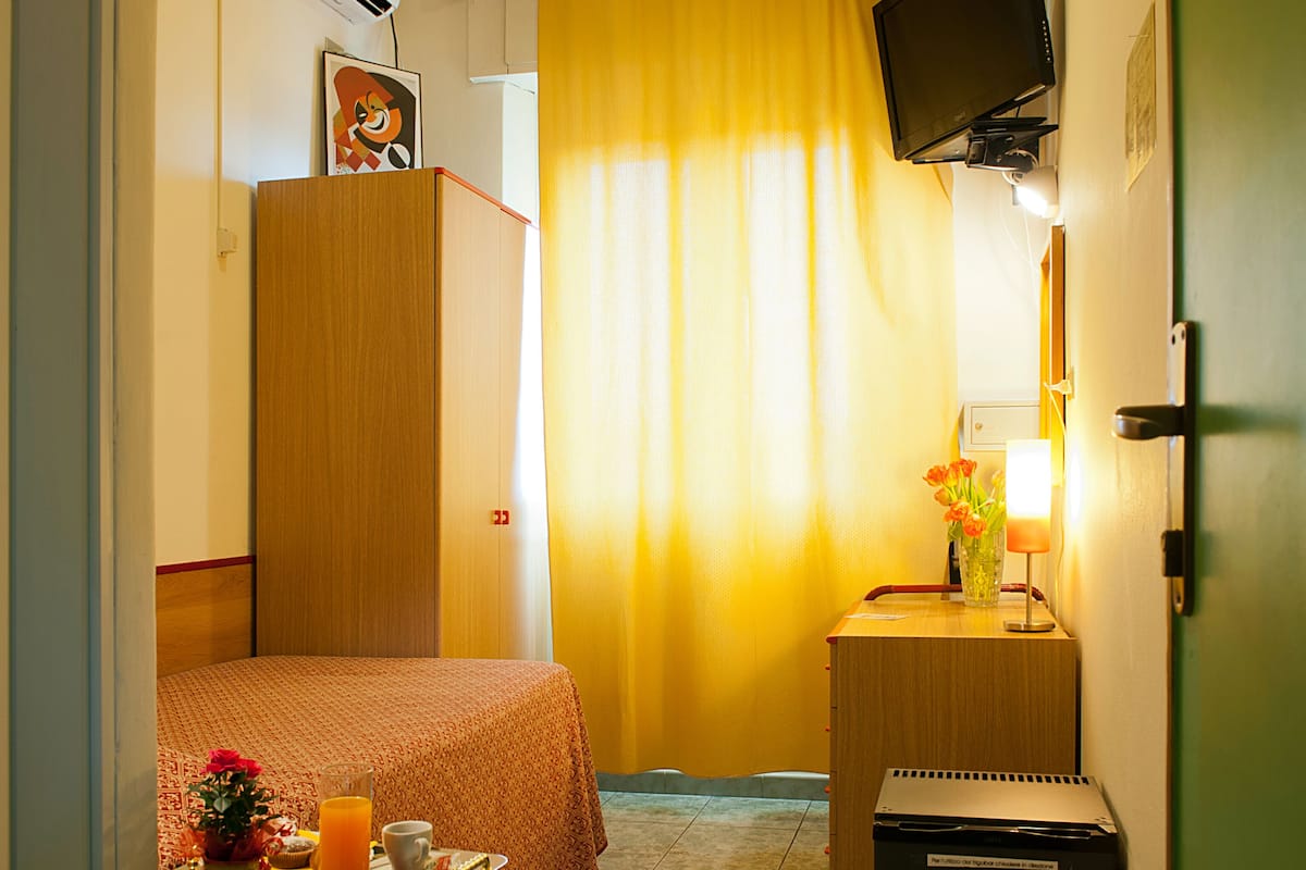 A hotel room with a bed, a desk with a lamp, a TV, and a small trash bin.