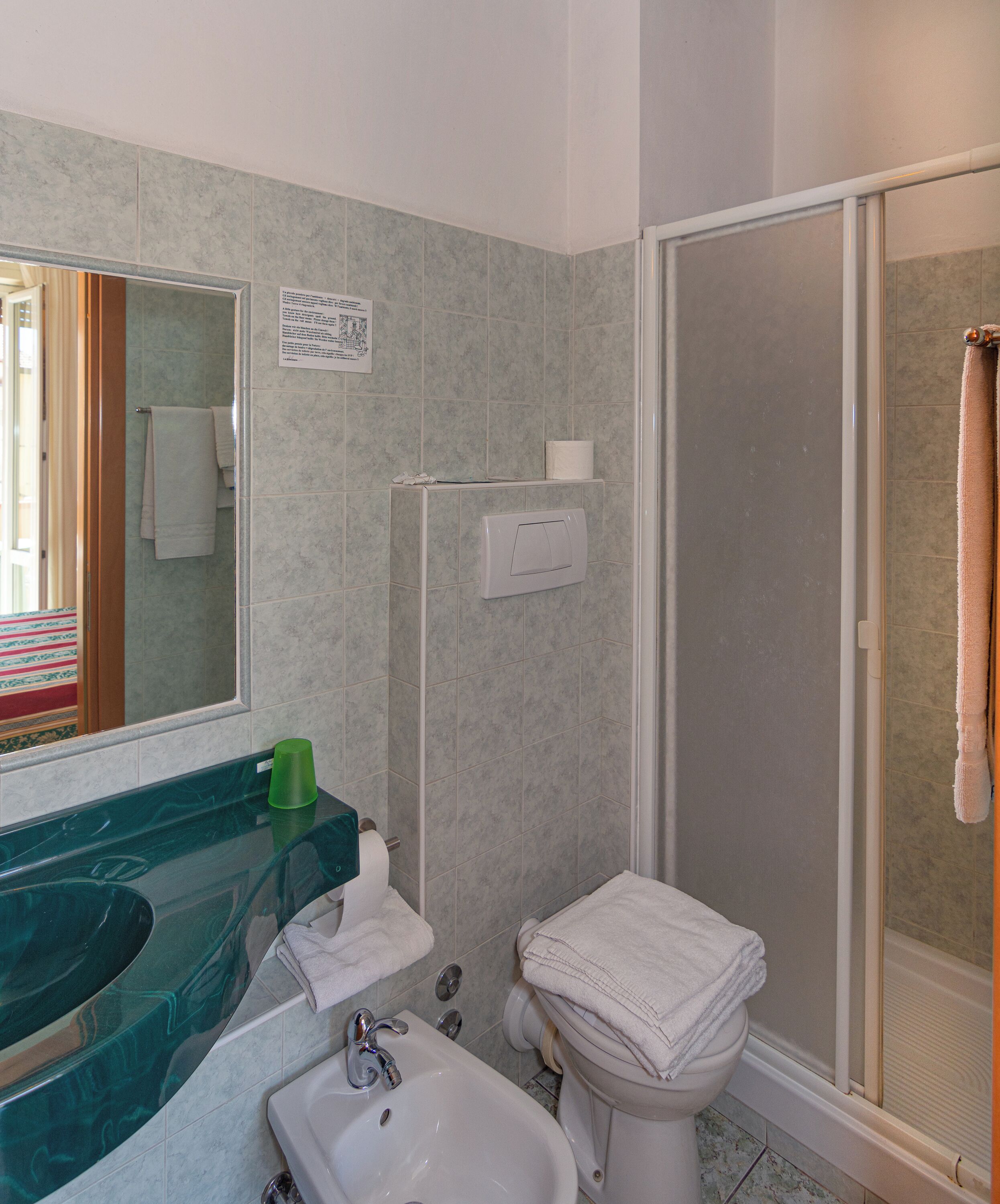 Een badkamer met een douchecabine van glas, een wastafel met een groene zeepdispenser en een toilet met een handdoek erop.